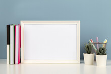 White Blank Wooden Mock Up Frame On White Desk With Paper Notebook, Books, Flowers At Home