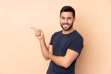 Wall Mural - Caucasian handsome man isolated on beige background pointing finger to the side