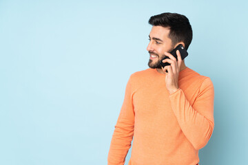 Canvas Print - Caucasian handsome man keeping a conversation with the mobile phone with someone over isolated blue background