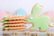 Close-up level shot of a rabbit-shaped cookie next to a stack of carrot-shaped cookies with shallow  depth of field showing soft-focus cookies to fore and rear, set on a light background.