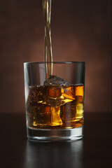 Wall Mural - Pouring whiskey into glass with ice cubes on table