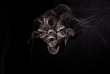 A Terrible Monster With Teeth Hangs On The Wall. Black Background. Sharp Teeth.