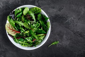 green mix salad leaves. healthy green salad with arugula in bowl on dark stone background.