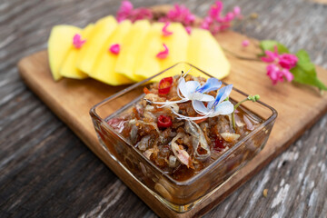 Close up of sweet fish sauce on the wooden plate with raw green mango slice. Special ingredient, red chili, onion, shrimp, fish sauce, sugar and shrimp paste. Thailand fruit season. Asia style