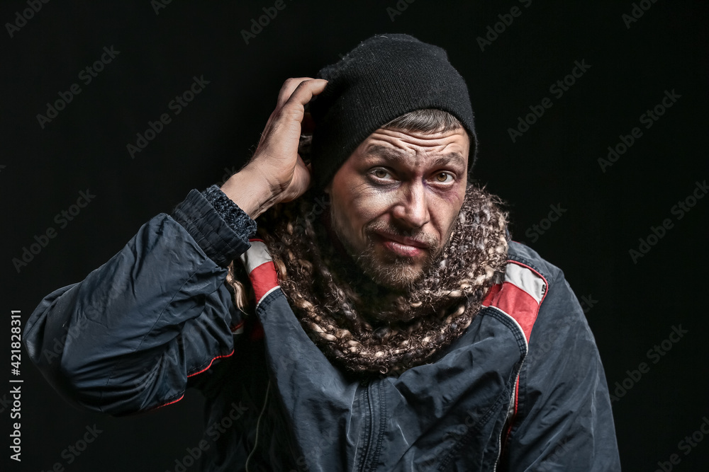 Portrait of confused homeless man on dark background