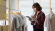 © ChayTee - Young attractive beautiful hipster asia female fashion store owner use digital tablet check stock clothes or package box on rail rack at home office small SME business entrepreneur e-commerce concept.