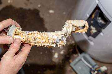 Repair and maintenance of boilers. The master plumber took it out of the boiler and holds in his hands a tubular electric heater covered with limescale