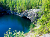 Fototapeta Na ścianę - a lake with blue water and a sheer cliff overgrown with forest, a grotto is visible in the rock above the water