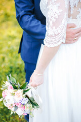 Wall Mural - the bride holds a bouquet in her lowered hand, the groom hugs her waist