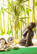 vista de un bodegón de un budha sobre un fondo de bambús con toallas , unas piedras y una palmera.