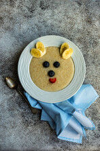 Overhead View Of A Bowl Of Oatmeal Decorated With Fresh Fruit To Look Like A Bear's Face