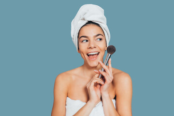 Wall Mural - Excited cheerful young woman in bath towel holding makeup brush