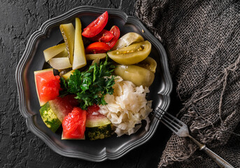 Wall Mural - Assorted pickled vegetables served on a plate. Top view of pickled tomatoes, watermelon, cucumbers, and cabbage on dark background. Preserved food