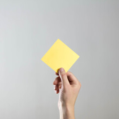 Wall Mural - The hand holds an empty square yellow sheet of paper. A clean flyer in your hands. For your text. Isolated on a gray background