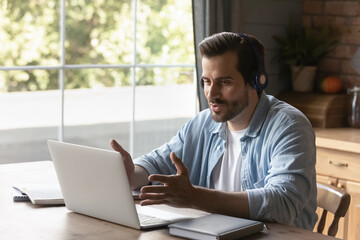 Canvas Print - Young Caucasian man wear headphones look at laptop screen talk speak on video call online. Millennial male in earphones use computer have webcam digital virtual conference. Technology concept.