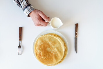 Men's hands with milk. There are a lot of pancakes on a white plate.