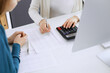 © Iryna - Accountant checking financial statement or counting by calculator income for tax form, hands close-up. Business woman sitting and working with colleague at the desk in office. Audit concept