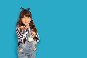 Cute fashion girl drinks nutritious delicious milk on a straw and stands on a blue background to copy space