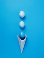 Wall Mural - Ice cream cone with blue gradient eggs on vibrant blue background. Minimal Easter or summer food concept. Trendy monochrome layout. Flat lay.