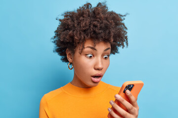 emotional surprised african american woman stares at smartphone screen reads amazing news with surpr