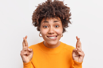 Wall Mural - Positive beautiful woman with Afro hair has big hopes in better waits for news puts efforts in ray bites lips crossed fingers for good luck prays wish come true isolated over white background