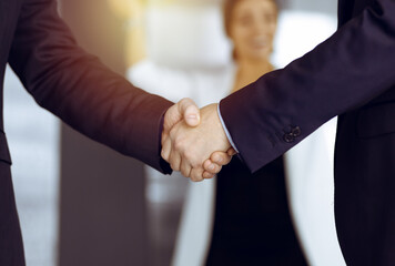 Unknown businesspeople are shaking their hands after signing a contract, while standing together in a sunny modern office, close-up. Business communication concept