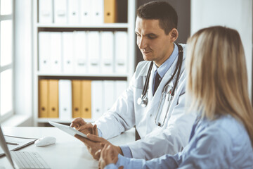 Unknown male doctor and patient woman discussing current health examination while sitting in clinic and using tablet computer. Perfect medical service in hospital. Medicine and healthcare concept