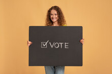 Smiling Young Redhead Curly Female Holding Holding Vote Sign, Poster Or Banner With Inscription