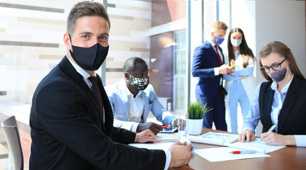 Wall Mural - Businessman in protective mask sitting in the office with his colleagues on a background.