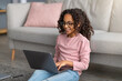 © Prostock-studio - E-learning concept. African american gen z girl using her laptop, doing homework, watching online course at home