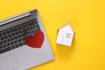 Mini paper house figurine and laptop, heart on yellow background. Flat lay