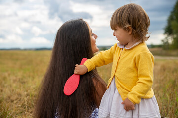 adorable toddler girl play combing her mom's hair outdoors outdoors on a sunny day