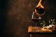 Pouring red wine into the glass against rustic dark wooden background