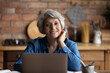 © fizkes - Headshot portrait of happy senior aged hispanic female sit at desk use laptop work study distantly. Confident old age woman remote worker freelancer look at camera at home office workplace at kitchen