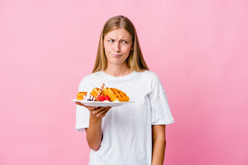 Wall Mural - Young russian woman eating a waffle isolated confused, feels doubtful and unsure.