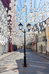 Decorations of Stoleshnikov lane in Moscow. Large garland from electric bulbs hangs above pedestrian street. Clear blue sky in the background. Travel in Russia theme.