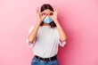 © Asier - Young caucasian woman wearing a mask for virus isolated on pink background showing okay sign over eyes