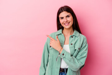 Young caucasian woman isolated on pink background smiling and pointing aside, showing something at blank space.