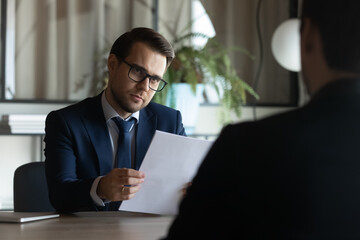 Sticker - Young Caucasian businessman listen to male job applicant candidate at interview in office. Business partners or clients consider collaboration partnership at briefing. Cooperation, employment concept.