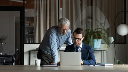 Wall Mural - serious diverse businessmen talk discuss business financial ideas working together on laptop in offi