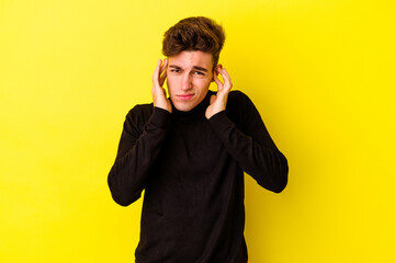 Wall Mural - Young caucasian man isolated on yellow background covering ears with fingers, stressed and desperate by a loudly ambient.