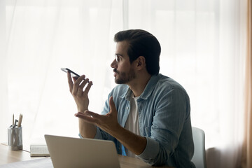 Wall Mural - Side view confident businessman wearing glasses recording voice message, holding smartphone, recording voice message for social network, chatting online or speakerphone, activating digital assistant