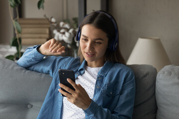 Close up smiling woman wearing headphones chatting on phone online, making video call, sitting on couch at home, talking with friends or relatives in social network, enjoying leisure time with gadget