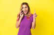 © luismolinero - Young woman using mobile phone over isolated yellow background thinking an idea pointing the finger up