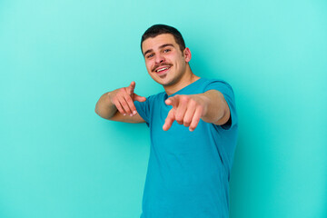 Young caucasian man isolated on blue background cheerful smiles pointing to front.