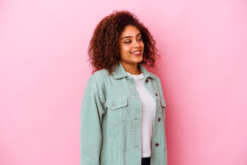 Young african american woman isolated on pink background looks aside smiling, cheerful and pleasant.