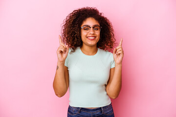 Young african american woman isolated on pink background indicates with both fore fingers up showing a blank space.