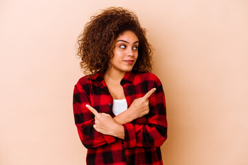 Wall Mural - Young african american woman isolated on beige background points sideways, is trying to choose between two options.