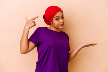 Wall Mural - Young african american woman isolated on beige background holding and showing a product on hand.