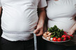 Overweight couple with healthy food and measure tape